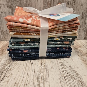 May include: A stack of fabric squares in various patterns and colors, including coral, teal, and navy. The fabric is tied with a white ribbon and a tag. The fabrics are stacked on a light wood surface.