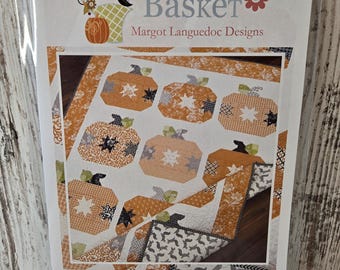 May include: A quilting pattern for a pumpkin pie quilt. The pattern features a patchwork design with orange, white, and black fabric. The pattern is titled "Pumpkin Pie" and includes the website address "www.thepatternbasket.com".