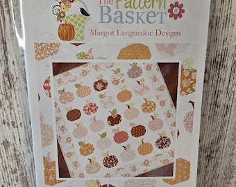 May include: A white paper pattern with a floral design and a pumpkin quilt block pattern. The pattern is titled "Pumpkin Charms" and is from "The Pattern Basket" by Margot Languedoc Designs. The website address is www.thepatternbasket.com.