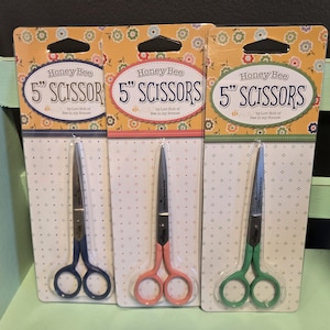 May include: Three packages of 5-inch Honey Bee scissors with colorful floral designs. Each package features a pair of scissors with blue, pink, or green handles.