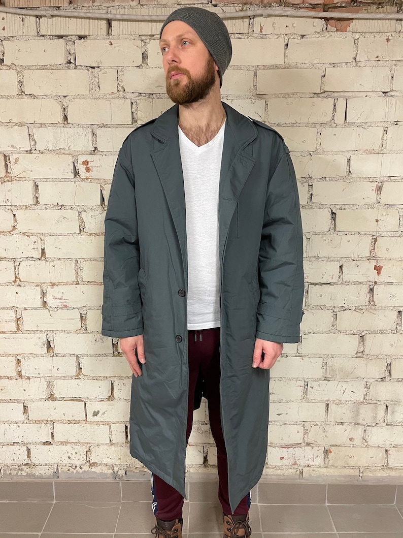 May include: A long, dark gray coat with a button closure and a collar. The coat has a relaxed fit and is made of a water-resistant material.