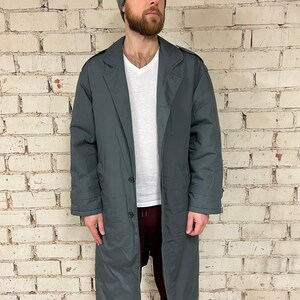May include: A long, dark gray coat with a button closure and a collar. The coat is made of a smooth, water-resistant fabric.