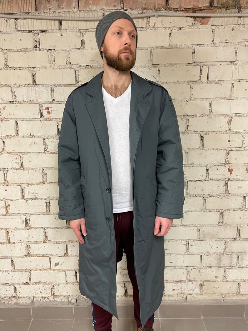May include: A long, dark gray coat with a button closure and a collar. The coat is made of a smooth, water-resistant fabric.