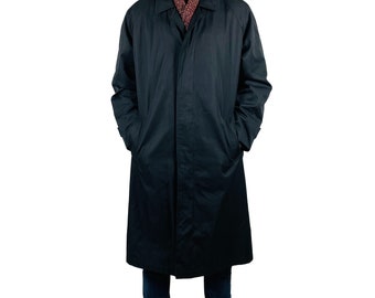 May include: A man wearing a long black coat, a gray beanie, and a burgundy scarf. He is wearing blue jeans and brown boots.