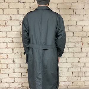 May include: A long, dark gray trench coat with a belt. The coat has a single-breasted closure and a collar.