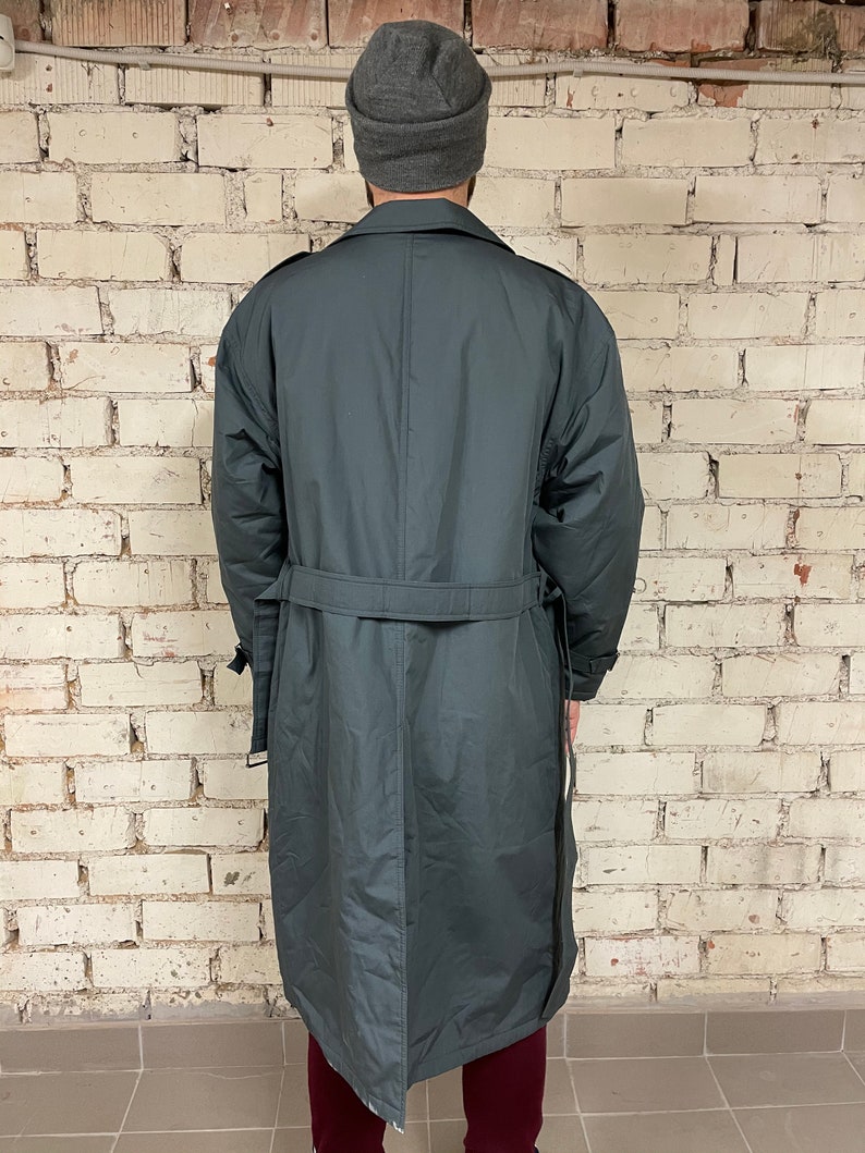 May include: A long, dark gray trench coat with a belt. The coat has a single-breasted closure and a collar.