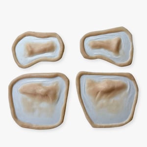 Puede incluir: Cuatro moldes de silicona para crear heridas falsas. Los moldes son de color beige y tienen un interior blanco. Cada molde tiene una forma y un tama&ntilde;o diferentes.