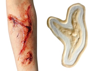 May include: A realistic fake wound for special effects makeup. The wound is a long, jagged cut with blood and dried blood. The wound is shown next to a silicone mold of the wound.