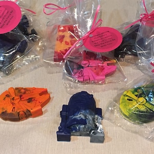 May include: Six individually wrapped Star Wars themed crayons. The crayons are shaped like the Millennium Falcon, R2-D2, and a TIE fighter. Each bag has a pink tag with the text "Thank you joining Charlotte's Rebellion against the First Order. May the Force Be With You."