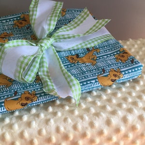 Puede incluir: Un papel de regalo azul turquesa y blanco con un patrón de lazo de cinta vichy verde y blanco. El patrón presenta imágenes de dibujos animados de Simba de El Rey León.