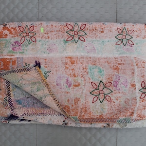 May include: Folded, vintage-style quilt with a floral pattern. The quilt features a patchwork design with a mix of colors, including orange, pink, green, and purple. The edges are finished with a stitched border. A decorative textile for the home.