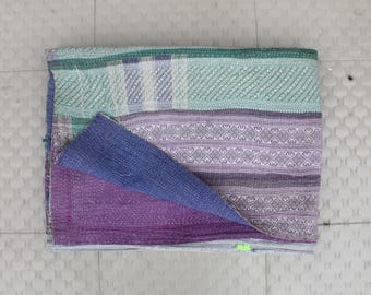 May include: A multi-colored kantha quilt with a patchwork design. The quilt is made of cotton and has a variety of colors, including purple, blue, and green. The quilt is folded in half and is lying on a white tiled surface.