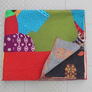 Può includere: Una trapunta patchwork con una varietà di colori e motivi. La trapunta presenta sezioni rosse, viola, verdi e blu. Il lato inferiore della trapunta è visibile, mostrando un tessuto grigio con un motivo floreale arancione.