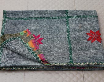 May include: A folded rectangular textile featuring a grey base with a fine dark grid pattern. It is accented by green embroidered lines forming a cross and red star-shaped motifs. The corner is folded back to reveal a colorful, multi-patterned lining.