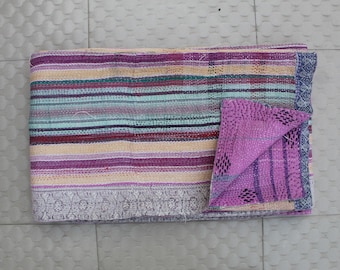 May include: A folded, multi-colored quilt with horizontal stripes in shades of purple, teal, and beige. A smaller, folded section of the quilt reveals a solid purple fabric with a dotted pattern. The quilt has a decorative border.