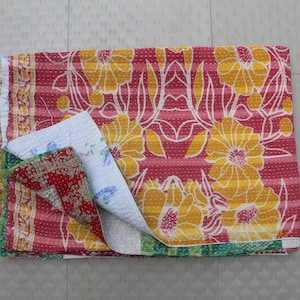 May include: A kantha quilt with a red, yellow, and white floral pattern. The quilt is folded in half and has a layered design.