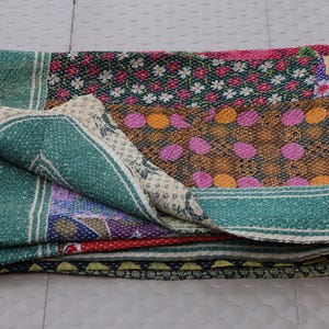 May include: A folded rectangular quilt featuring a patchwork of various fabrics with intricate kantha stitching. The design includes panels of green, pink, yellow, and dark blue, decorated with floral, geometric, and polka dot patterns throughout.