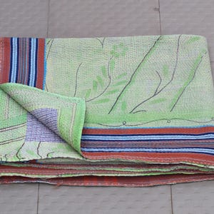 Könnte beinhalten: Eine gefaltete, hellgrüne Kantha-Steppdecke mit floralem Design und einer gefalteten Ecke. Die Steppdecke hat einen Rand mit roten, blauen und weißen Streifen. Die Steppdecke ist aus weichem, genähtem Stoff gefertigt.