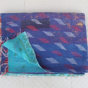 May include: A folded, reversible quilt with a blue background and a geometric pattern of red and white diamonds. The reverse side is turquoise. The edges have a fringed trim.