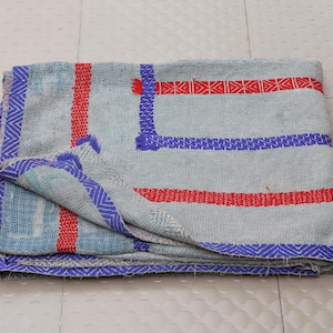 May include: A folded textile blanket featuring a light gray base with prominent horizontal and vertical stripes in vibrant red and deep blue. The fabric displays a textured surface with visible stitching patterns throughout the material.