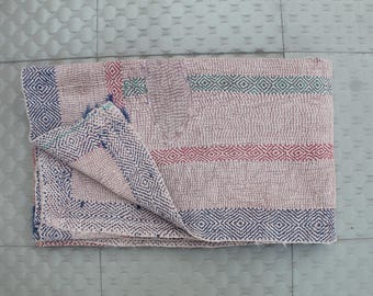 Puede incluir: Textil beige plegado con un patrón geométrico. Los bordes y las rayas presentan diseños de diamantes azules, rojos y verdes. El textil está doblado, revelando el borde estampado y el diseño a rayas.