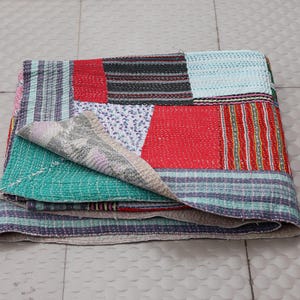 Könnte beinhalten: Eine gefaltete Patchwork-Decke mit verschiedenen rechteckigen Stoffbahnen in Rot, Türkis, Hellblau und Schwarz mit weißen Blumen- und Streifenmustern. Das Textil weist auf der gesamten Oberfläche sichtbare Steppstichdetails auf.