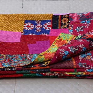 Könnte beinhalten: Eine gefaltete Patchwork-Decke mit einer Vielzahl bunter Stoffquadrate mit komplizierten Mustern, darunter Blumen-, Paisley- und geometrische Designs in Rot-, Gelb-, Rosa-, Blau- und Grüntönen, veredelt mit sichtbaren Steppstichen.
