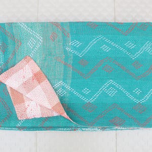 Puede incluir: Un edredón turquesa y coral con un patrón geométrico. El edredón presenta un diseño en zigzag repetido en blanco y coral, con una sección estampada en coral y blanco doblada.