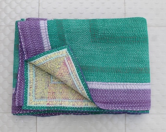 May include: A folded, handmade quilt in green and purple. The quilt has a detailed, stitched pattern and a contrasting patterned border. The interior fabric is a mix of yellow, pink, and green.