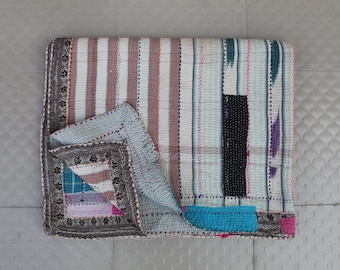 Puede incluir: Una colcha kantha de rayas blancas y marrones con detalles azules y morados. La colcha está doblada por la mitad y tiene un borde decorativo.