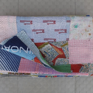 Puede incluir: Una colcha de retazos con una variedad de colores y patrones, incluyendo azul, rosa, rojo y blanco. La colcha está hecha de diferentes telas cosidas juntas para crear un diseño único. La colcha está doblada por la mitad y colocada sobre una superficie gris.