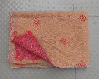 May include: A folded, reversible blanket with a peach-colored exterior featuring red diamond patterns. The interior is a vibrant pink with a textured design. The blanket is made of a soft, woven material.