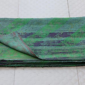 May include: A rectangular textile piece featuring a layered design with a vibrant green top layer and a dark navy blue base layer. The fabric displays a visible stitched texture throughout, with one corner folded over to reveal the contrasting dark underside.