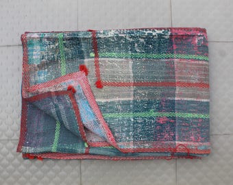 May include: A patchwork quilt with a plaid pattern in shades of blue, green, red, and white. The quilt is folded in half and has a frayed edge.