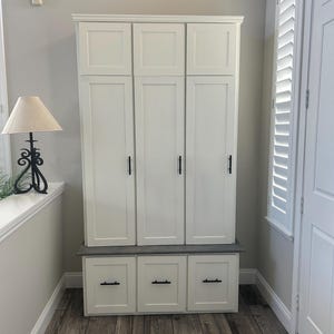 May include: White wooden cabinet with three doors and three drawers. The cabinet has black hardware and a gray countertop. The cabinet is in a hallway with wood-look tile flooring.