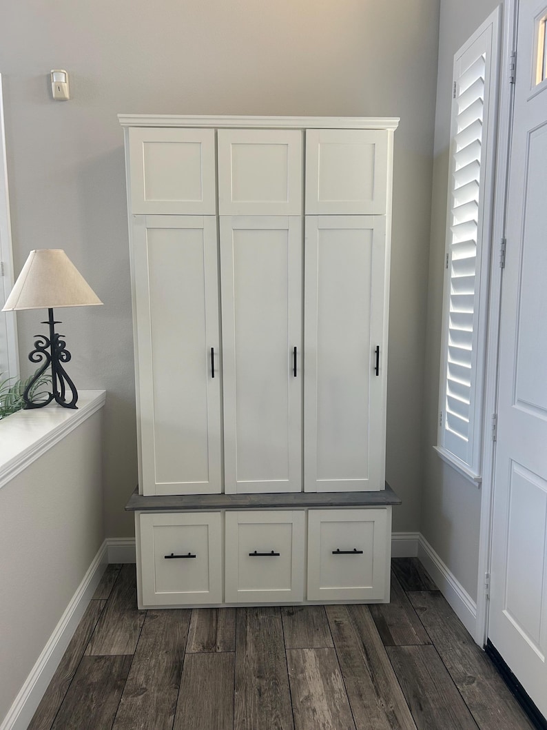 May include: White wooden cabinet with three doors and three drawers. The cabinet has black hardware and a gray countertop. The cabinet is in a hallway with wood-look tile flooring.