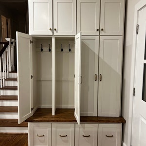 May include: White wooden cabinet with two doors and three drawers. The cabinet has a shelf and hooks inside. The cabinet is open and the interior is visible.