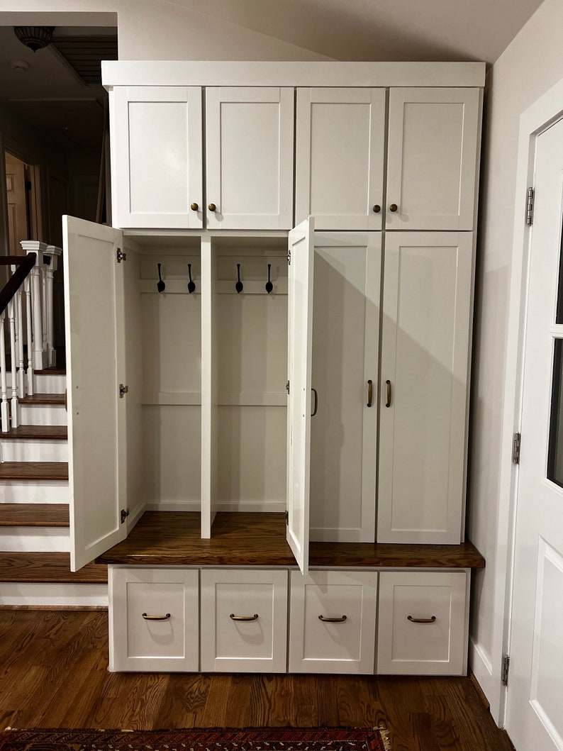 May include: White wooden cabinet with two doors and three drawers. The cabinet has a shelf and hooks inside. The cabinet is open and the interior is visible.