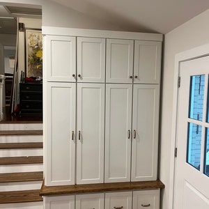 May include: White cabinet with six doors and four drawers. The cabinet has a wooden top and is made of wood. The cabinet is in a room with a wooden floor and a staircase.
