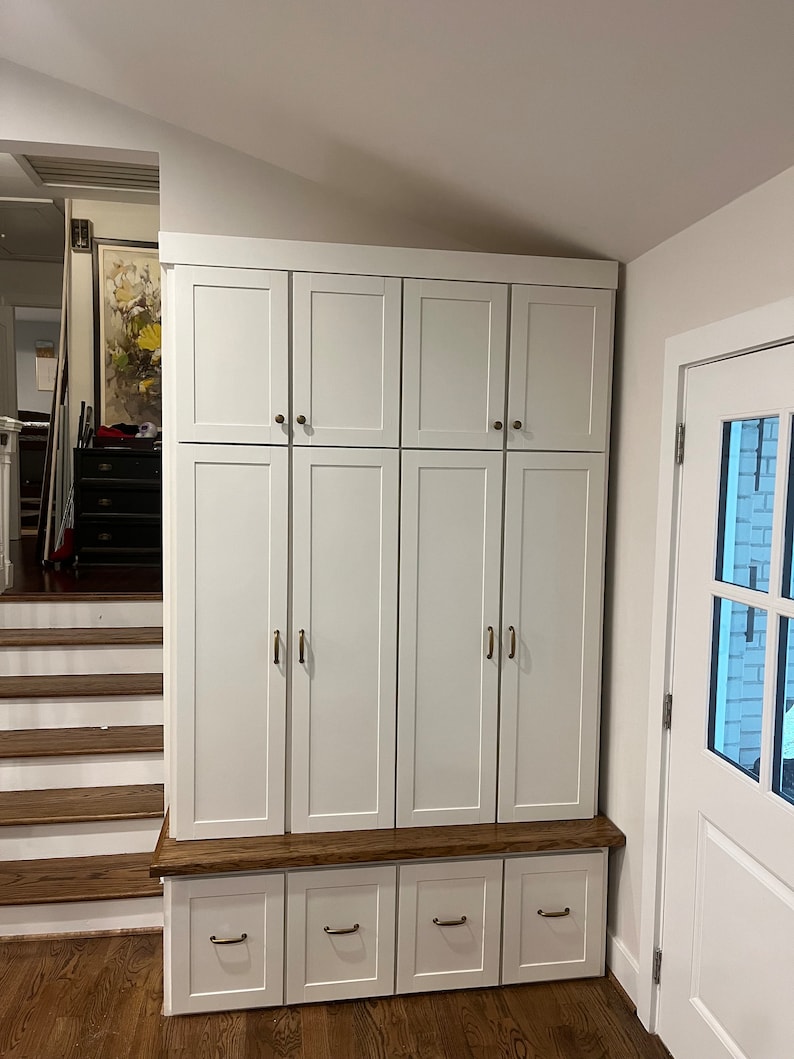 May include: White cabinet with six doors and four drawers. The cabinet has a wooden top and is made of wood. The cabinet is in a room with a wooden floor and a staircase.