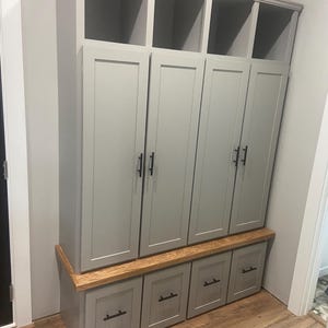 May include: A gray wooden storage cabinet with four doors and three drawers. The cabinet has a light wood top and is sitting on a wood floor.