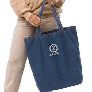 May include: A person is carrying a blue denim tote bag with a white embroidered logo that says "full throttle" and a cartoon face inside a circle.