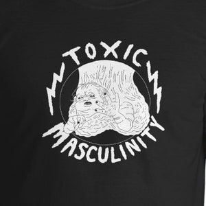 Könnte beinhalten: Schwarzes T-Shirt mit einem weißen Grafikdruck eines Kreises mit den Worten "Toxic Masculinity" und einem Blitz auf jeder Seite. Im Inneren des Kreises befindet sich eine Zeichnung einer Kreatur mit mehreren Augen.