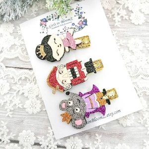 May include: Set of four glitter hair clips featuring characters from The Nutcracker. The characters include a ballerina, a nutcracker soldier, a mouse king, and a sugar plum fairy. The clips are made of felt and glitter and have gold-coloured clips.