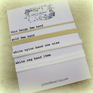 May include: A white card displays four hair bands: a thin beige 3mm band, a gold 9mm band, a white nylon band, and a white 15mm band. The card has the text "Girls in BloomZ" and "GirlsinBloomZ.etsy.com".