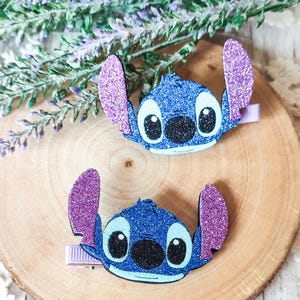 May include: Two blue and purple glitter Stitch character hair clips. The clips are shaped like Stitch's head with big eyes and a wide smile.