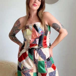 May include: A strapless top and wide-leg pants set made from a patchwork of various fabrics in red, green, black, yellow, and white. The garment features visible zigzag stitching connecting the diverse textile squares and patterns throughout the set.