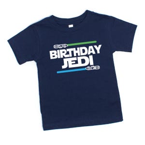 May include: A navy blue t-shirt with the text "Birthday Jedi" in white, with green and blue lightsaber graphics.