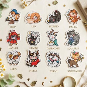 May include: A collection of twelve die-cut stickers featuring cartoon cats dressed as zodiac signs, including Libra, Leo, Scorpio, Pisces, Cancer, Gemini, Capricorn, Aquarius, Aries, Taurus, Virgo, and Sagittarius, each labelled with its name.