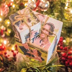 May include: A stack of wooden cubes featuring photographs of a couple on their wedding day. The cubes are tied together with twine and are sitting on a glass jar filled with greenery.